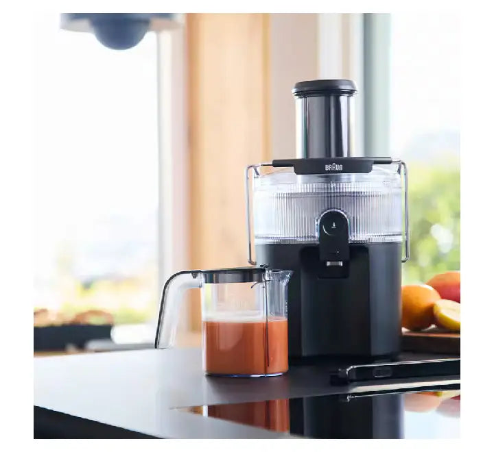 Braun MultiJuice 5 Spin Juicer SJ5000BK in matte black on a kitchen counter next to a clear juice pitcher filled with fresh orange juice.